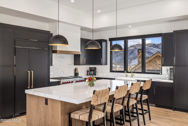 kitchen featuring tasteful backsplash, light stone countertops, light wood-type flooring, a kitchen bar, and hanging light fixtures