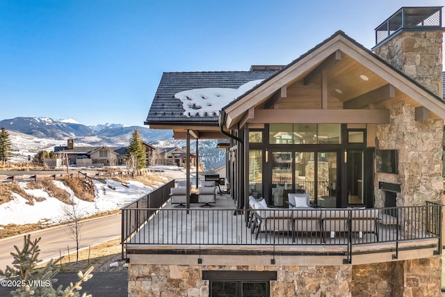 snow covered house featuring a mountain view, stone siding, and a chimney