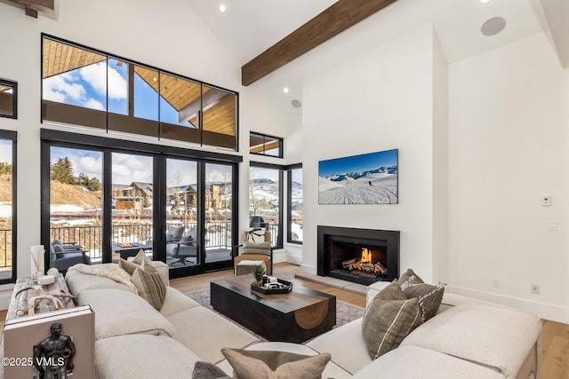 living room with baseboards, a lit fireplace, beam ceiling, wood finished floors, and high vaulted ceiling