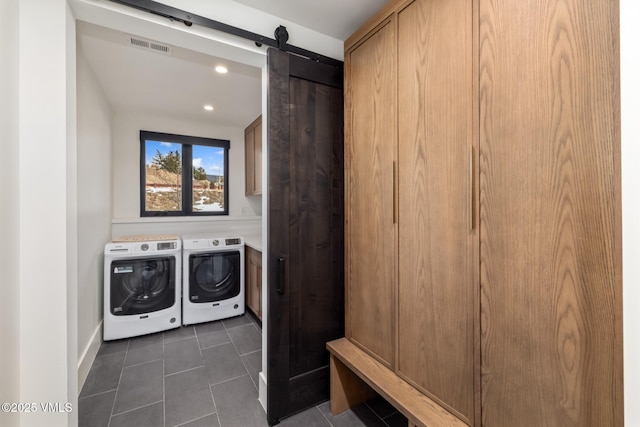 laundry room featuring visible vents, dark tile patterned flooring, washer and clothes dryer, a barn door, and cabinet space