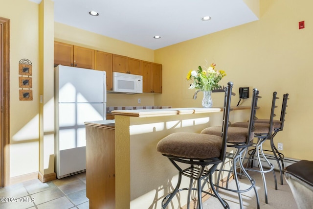 kitchen with light tile patterned flooring, a breakfast bar, white appliances, and kitchen peninsula