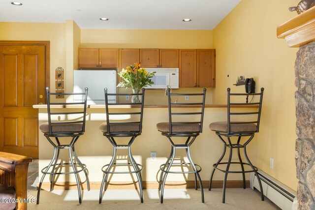 kitchen featuring white appliances, a baseboard radiator, a breakfast bar, and light colored carpet