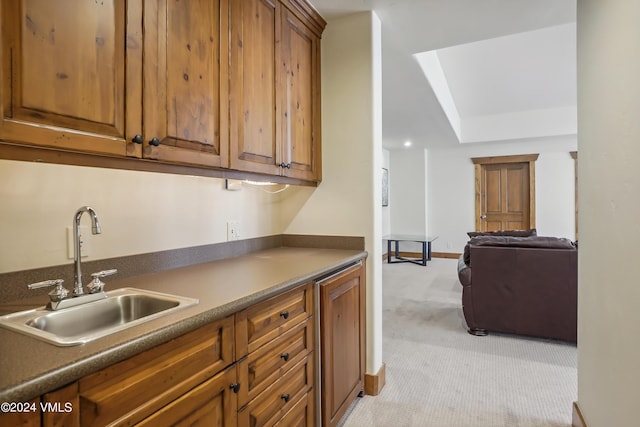 kitchen featuring brown cabinets, dark countertops, light colored carpet, and a sink