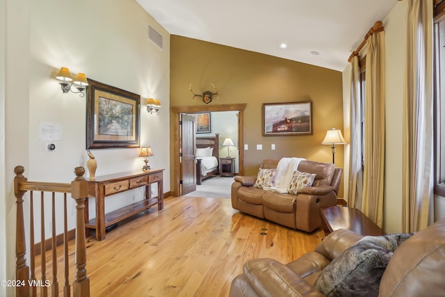 living area featuring light wood-style floors, baseboards, visible vents, and vaulted ceiling