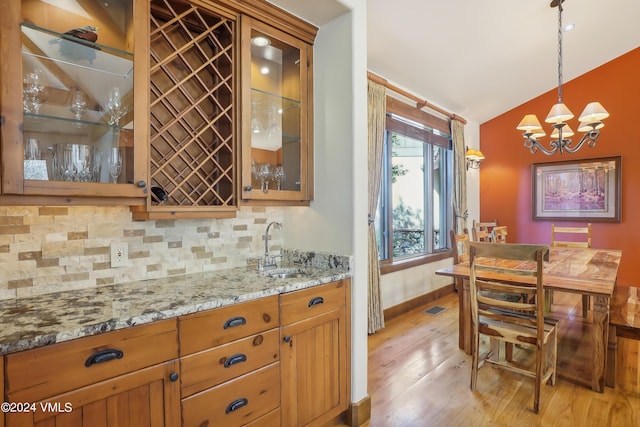 kitchen with glass insert cabinets, hanging light fixtures, light stone countertops, vaulted ceiling, and a sink