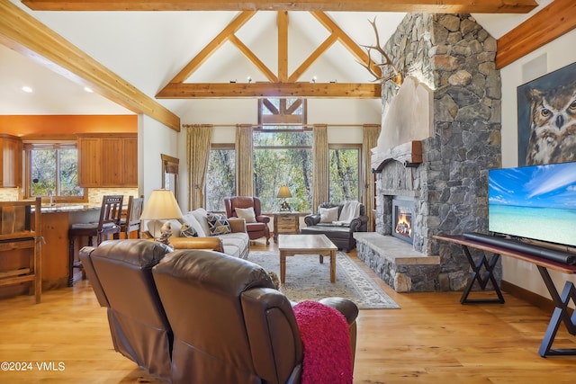 living area featuring high vaulted ceiling, a stone fireplace, beamed ceiling, and light wood-style flooring