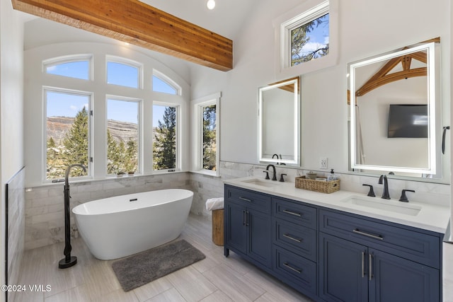 bathroom with tile walls, vaulted ceiling with beams, a bathtub, vanity, and a mountain view