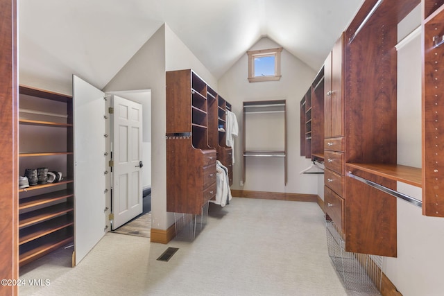 walk in closet with vaulted ceiling and light colored carpet