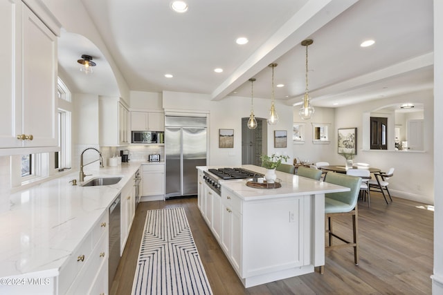 kitchen with a kitchen island, appliances with stainless steel finishes, beamed ceiling, sink, and white cabinets