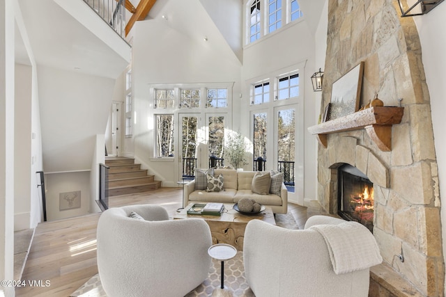 living room featuring a high ceiling, plenty of natural light, a stone fireplace, and light hardwood / wood-style flooring