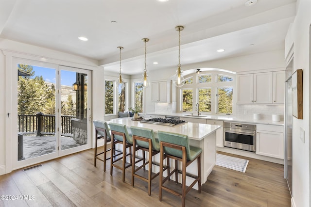 kitchen with hardwood / wood-style flooring, stainless steel appliances, white cabinets, a kitchen island, and decorative light fixtures