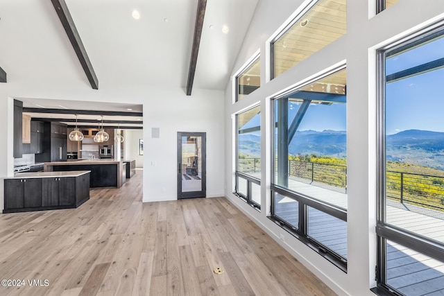 unfurnished living room featuring a high ceiling, a mountain view, light wood-type flooring, and beam ceiling