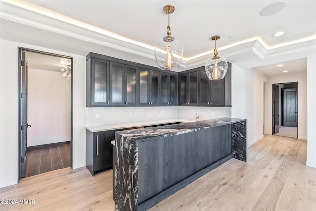 kitchen featuring hanging light fixtures, backsplash, light hardwood / wood-style floors, a raised ceiling, and dark stone counters