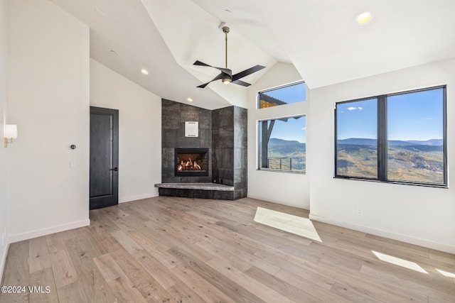 unfurnished living room with a tiled fireplace, ceiling fan, high vaulted ceiling, and light hardwood / wood-style floors