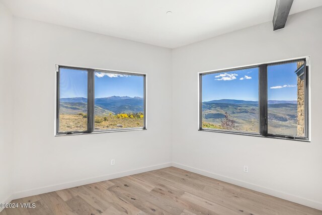 unfurnished room featuring a mountain view, beam ceiling, and light hardwood / wood-style flooring