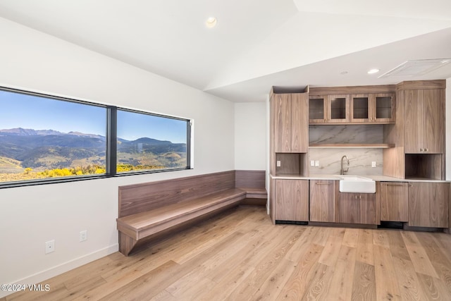 kitchen with sink, tasteful backsplash, a mountain view, vaulted ceiling, and light wood-type flooring