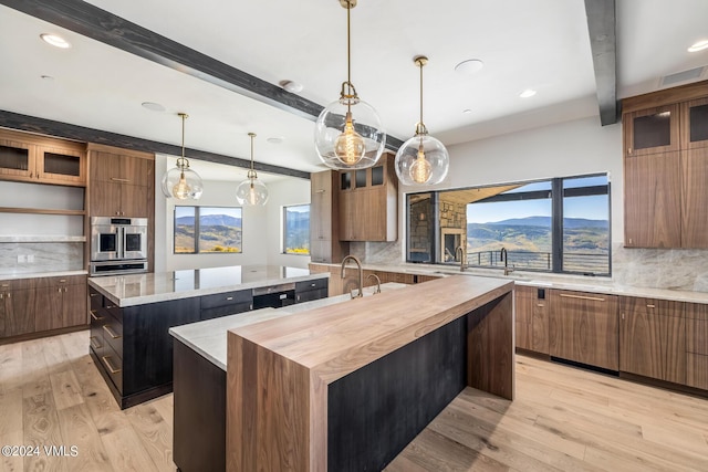 kitchen with hanging light fixtures, light wood-type flooring, beamed ceiling, a kitchen island with sink, and backsplash