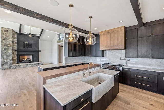 kitchen featuring a kitchen island with sink, pendant lighting, light hardwood / wood-style floors, and a large fireplace