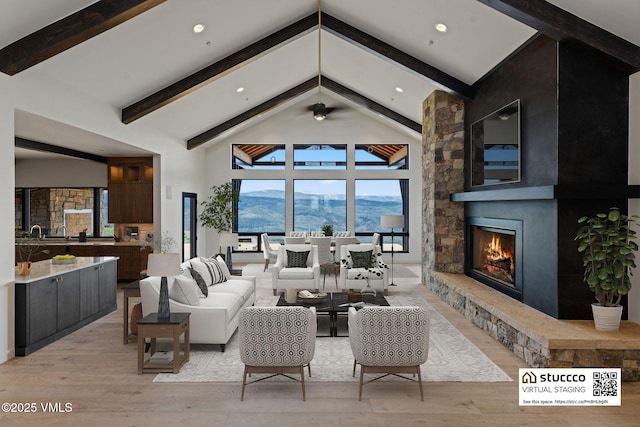 living room with high vaulted ceiling, a mountain view, a stone fireplace, beamed ceiling, and light wood-type flooring