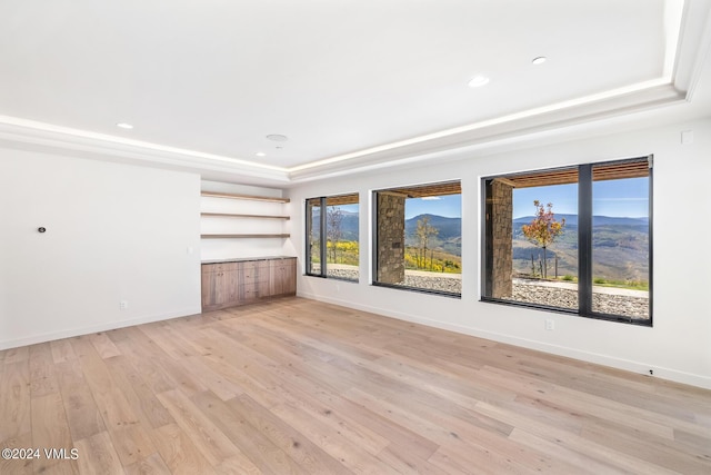 unfurnished living room featuring a raised ceiling, light wood-type flooring, and a mountain view