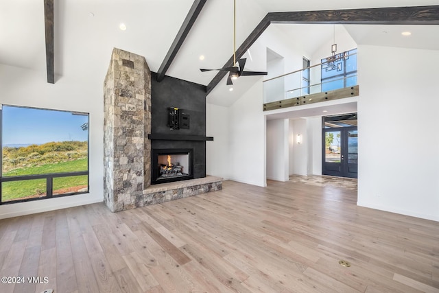 unfurnished living room with a stone fireplace, high vaulted ceiling, ceiling fan, beam ceiling, and light hardwood / wood-style floors