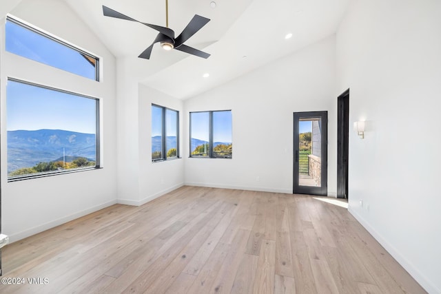 empty room featuring a mountain view, a healthy amount of sunlight, high vaulted ceiling, and light hardwood / wood-style floors