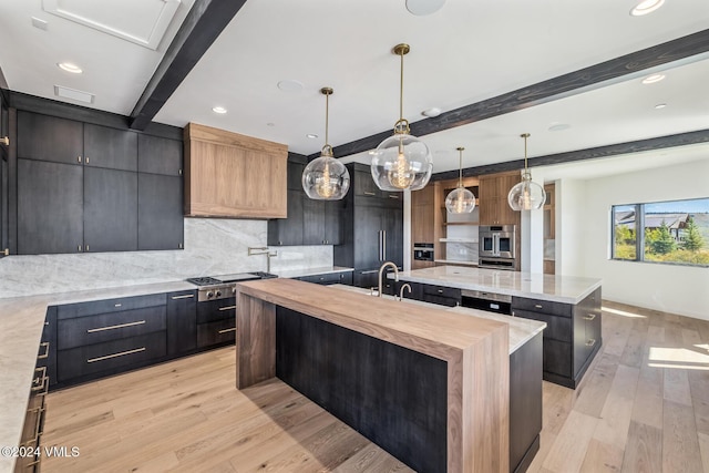 kitchen with pendant lighting, a kitchen island with sink, backsplash, beamed ceiling, and stainless steel gas stovetop