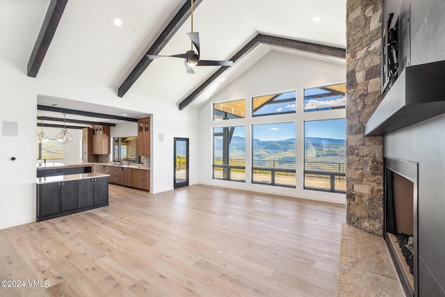 unfurnished living room featuring a stone fireplace, high vaulted ceiling, sink, light hardwood / wood-style floors, and a mountain view