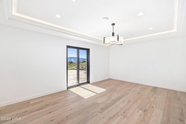 unfurnished dining area with a tray ceiling, a chandelier, and light wood-type flooring