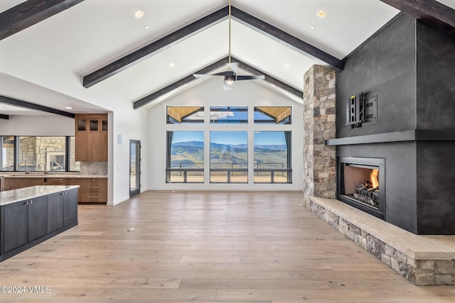 unfurnished living room featuring a stone fireplace, light hardwood / wood-style flooring, high vaulted ceiling, and beamed ceiling