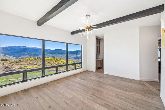 spare room featuring beamed ceiling, a mountain view, a notable chandelier, and light hardwood / wood-style flooring