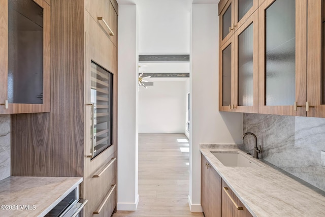 kitchen featuring sink, light stone counters, beverage cooler, light hardwood / wood-style floors, and backsplash