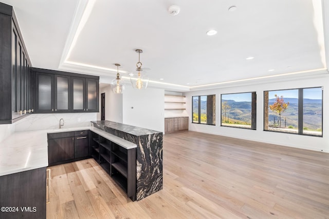 kitchen featuring decorative light fixtures, light hardwood / wood-style flooring, kitchen peninsula, and a raised ceiling