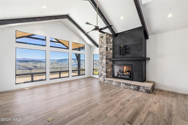 unfurnished living room with hardwood / wood-style floors, high vaulted ceiling, a mountain view, a stone fireplace, and beamed ceiling