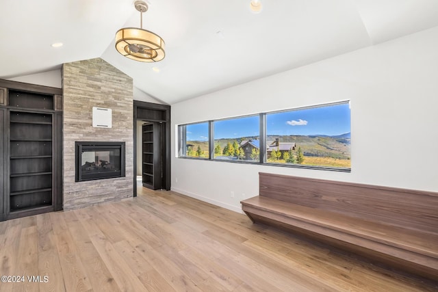 unfurnished living room featuring a multi sided fireplace, a mountain view, vaulted ceiling, and light wood-type flooring