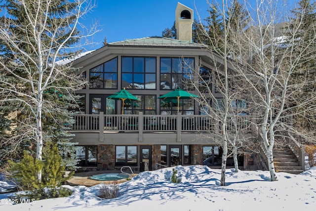 snow covered back of property with a wooden deck, an in ground hot tub, a chimney, and stairs