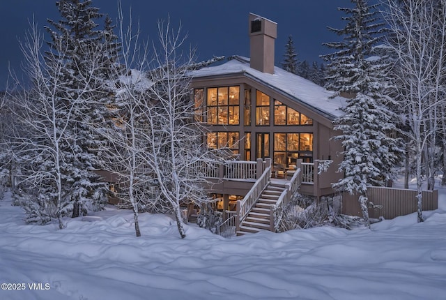 snow covered rear of property with stairway and a chimney