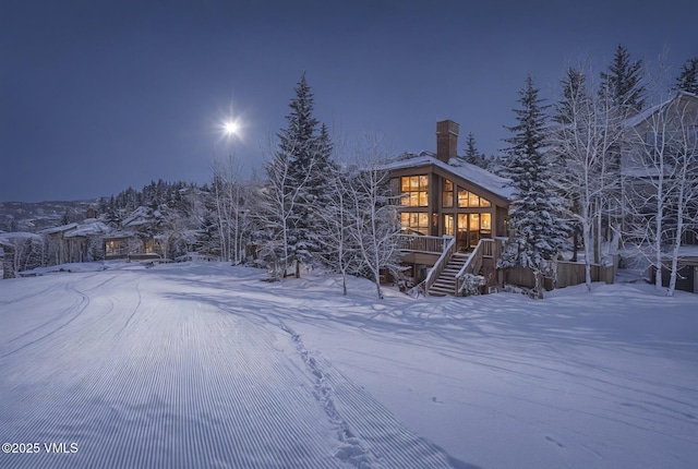 snow covered house with stairway, a chimney, and a wooden deck