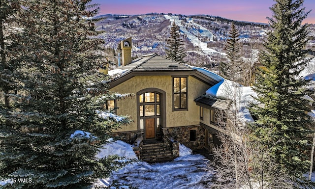 chalet / cabin with stone siding, stucco siding, a mountain view, and a chimney