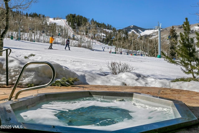 snow covered pool with an in ground hot tub and a mountain view