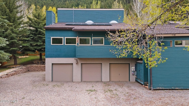 view of front facade with solar panels, an attached garage, a chimney, a view of trees, and stucco siding