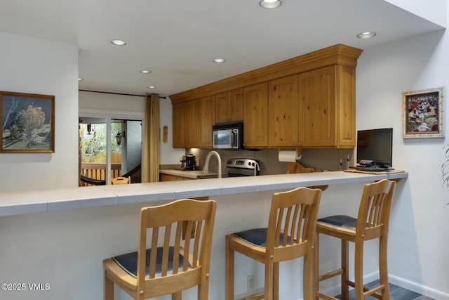 kitchen featuring stainless steel appliances, tile counters, recessed lighting, backsplash, and a breakfast bar