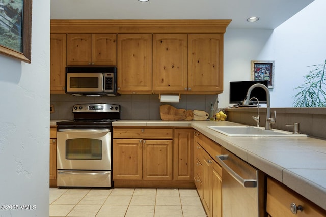 kitchen featuring appliances with stainless steel finishes, a sink, backsplash, tile counters, and recessed lighting