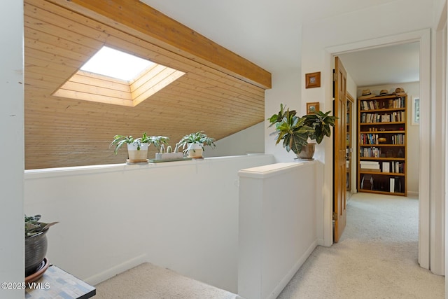hallway with an upstairs landing, carpet, a skylight, and vaulted ceiling