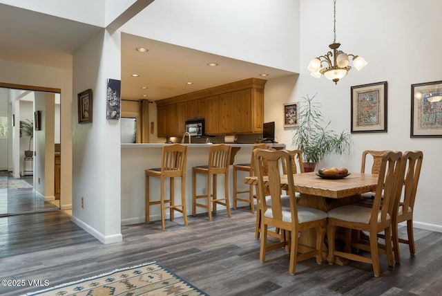 dining room with dark wood finished floors, baseboards, a chandelier, recessed lighting, and a high ceiling
