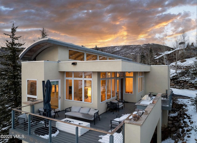 snow covered back of property with a deck with mountain view and an outdoor hangout area