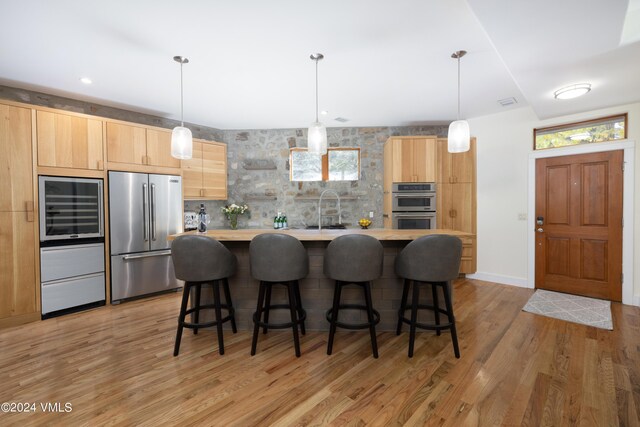 kitchen featuring pendant lighting, stainless steel appliances, a kitchen island, and light brown cabinets