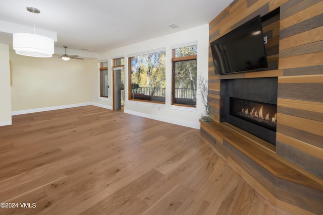 unfurnished living room with ceiling fan, a large fireplace, and wood-type flooring