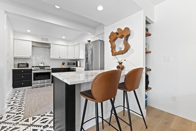 1151 Casolar Del Norte Dr Unit A, Vail, CO 81657 - kitchen featuring appliances with stainless steel finishes, white cabinetry, a kitchen breakfast bar, a peninsula, and tasteful backsplash