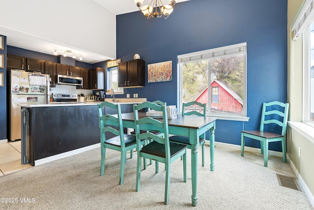 dining space featuring a chandelier, high vaulted ceiling, light colored carpet, and plenty of natural light